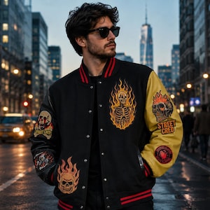 May include: A black varsity jacket with red striped ribbed trim, featuring yellow sleeves and multiple graphic patches. The patches include flaming skulls, a skeleton torso, and text reading STREET CRED. The jacket has a snap-button front closure.