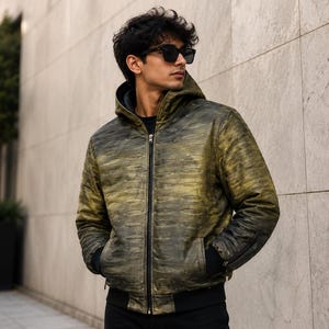 May include: A hooded jacket featuring a distressed olive green and black gradient finish with a textured, horizontal slash-like pattern. The jacket includes a central black zip, black ribbed cuffs, a black ribbed hem, and a solid black inner lining.