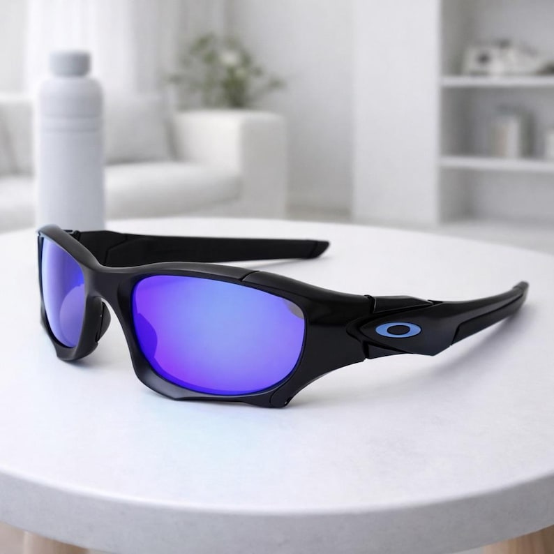 May include: Black sunglasses with blue mirrored lenses. The sunglasses have a sporty design with a curved frame and a small blue logo on the temple. The lenses reflect a vibrant blue color.