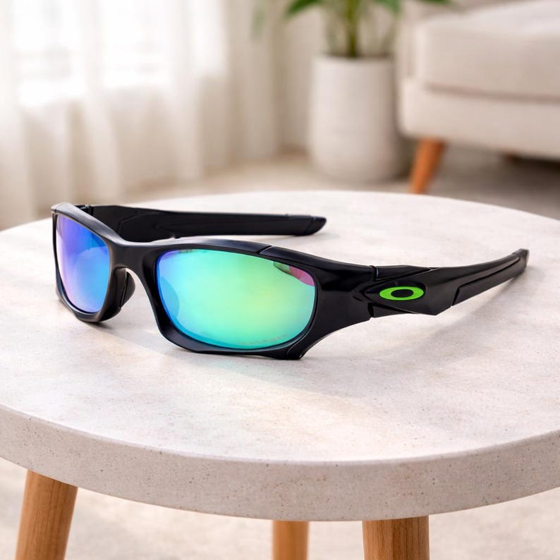 May include: Black sunglasses with iridescent lenses, resting on a white table. The sunglasses have a sleek, modern design with a green logo on the temple. The lenses reflect a mix of blue and green hues.