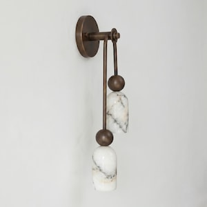 May include: A wall-mounted light fixture with a bronze finish. The fixture features two white marble-like pendants with dark veining, suspended from a bronze arm. The fixture is designed for indoor use and adds a touch of elegance.