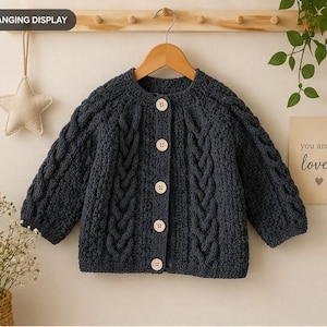 May include: A dark charcoal grey long-sleeve cardigan featuring a textured cable knit pattern on the front and sleeves. The garment has a round neckline and is fastened with five light-coloured wooden buttons down the centre front placket.