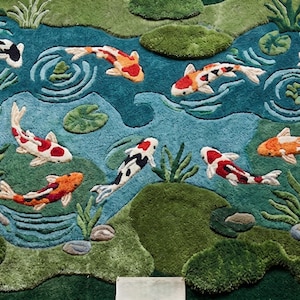 May include: A decorative rug featuring a pond scene with colorful koi fish. The rug has a teal blue pond with green and brown accents, and the koi fish are orange, red, black, and white. The rug is designed to resemble a natural pond setting.