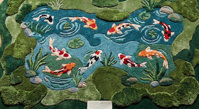 May include: A decorative rug featuring a pond scene with colorful koi fish. The rug has a teal blue pond with green and brown accents, and the koi fish are orange, red, black, and white. The rug is designed to resemble a natural pond setting.