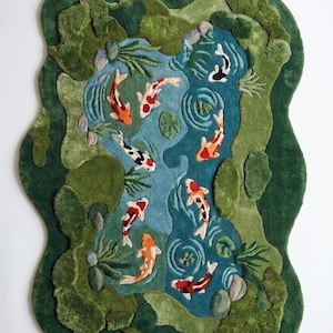 May include: A handcrafted rug depicting a koi pond scene. The rug features a blue pond with koi fish in shades of orange, red, black, and white. The pond is surrounded by green, textured foliage and rocks, creating a three-dimensional effect.