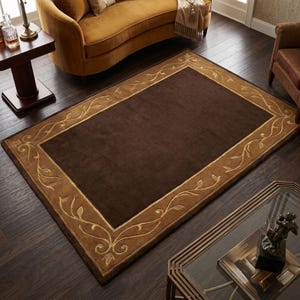 May include: A rectangular area rug featuring a solid dark brown centre panel surrounded by a wide tan border. The border is decorated with a continuous, symmetrical vine and leaf pattern in a lighter tan tone, framing the dark brown interior.