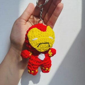 Peut inclure: Un porte-cl&eacute;s en crochet repr&eacute;sentant un personnage avec une combinaison rouge et jaune, un masque facial jaune avec des fentes oculaires blanches et un petit d&eacute;tail circulaire blanc sur la poitrine, fix&eacute; &agrave; un anneau en m&eacute;tal argent&eacute;.