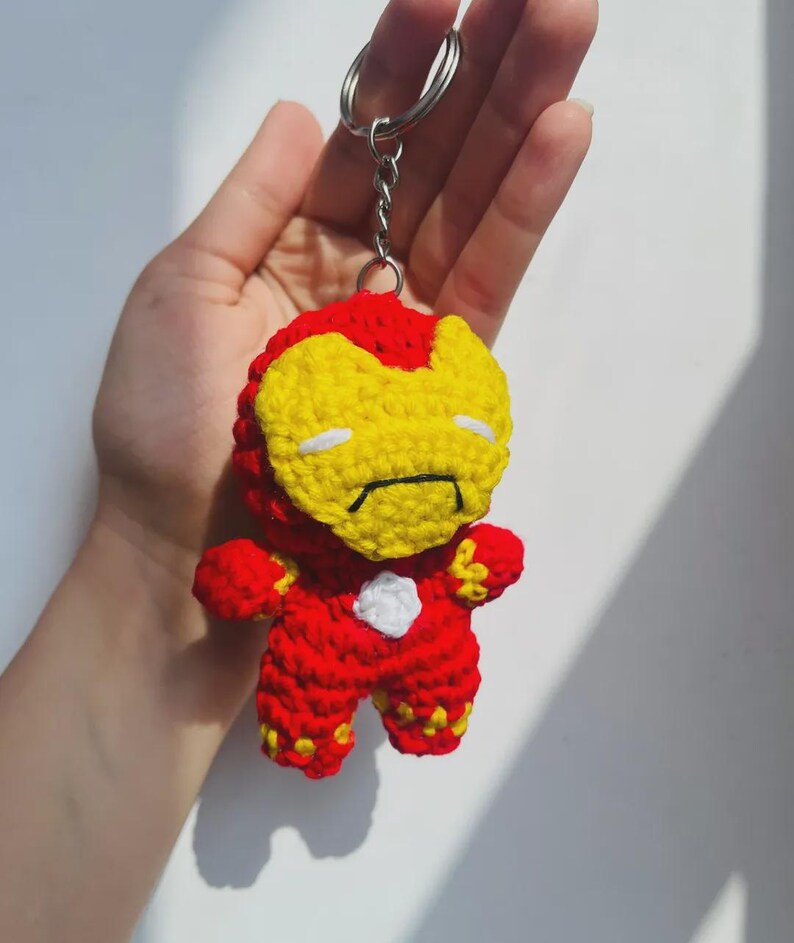 Peut inclure: Un porte-cl&eacute;s en crochet repr&eacute;sentant un personnage avec une combinaison rouge et jaune, un masque facial jaune avec des fentes oculaires blanches et un petit d&eacute;tail circulaire blanc sur la poitrine, fix&eacute; &agrave; un anneau en m&eacute;tal argent&eacute;.
