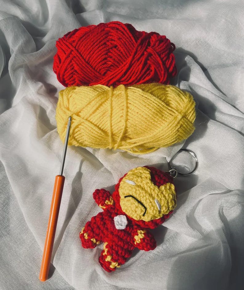 Peut inclure: Un porte-cl&eacute;s personnage crochet&eacute; rouge et jaune avec un masque, un embl&egrave;me de poitrine blanc, des pelotes de laine assorties rouge et jaune, et un crochet en m&eacute;tal avec un manche orange pour les projets manuels.