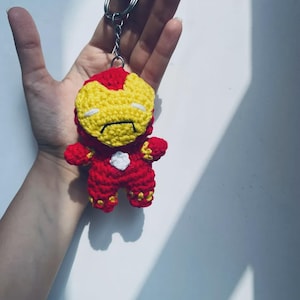 Peut inclure: Un petit porte-cl&eacute;s en crochet fait main repr&eacute;sentant un personnage avec une combinaison rouge et jaune, un masque facial jaune et un petit d&eacute;tail circulaire blanc sur la poitrine. La figurine est fix&eacute;e &agrave; un anneau en m&eacute;tal argent&eacute;.