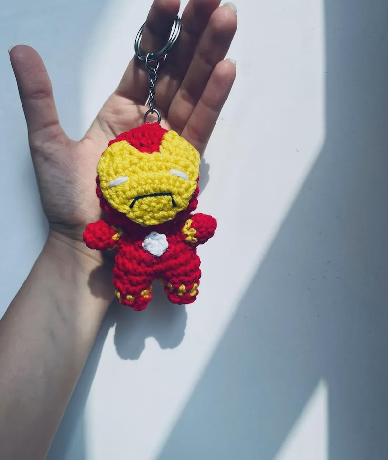 Peut inclure: Un petit porte-cl&eacute;s en crochet fait main repr&eacute;sentant un personnage avec une combinaison rouge et jaune, un masque facial jaune et un petit d&eacute;tail circulaire blanc sur la poitrine. La figurine est fix&eacute;e &agrave; un anneau en m&eacute;tal argent&eacute;.