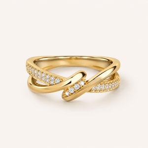 Peut inclure: Une bague dorée au design unique et entrelacé. La bague présente un anneau orné d'une série de petites pierres scintillantes serties sur le dessus. Le design de la bague est moderne et élégant, adapté au quotidien ou aux occasions spéciales.