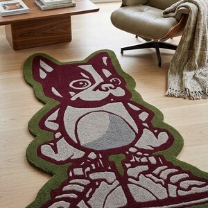 Könnte beinhalten: Dekorativer Teppich mit einem Cartoon-Hund-Design. Der Teppich hat einen grünen Rand mit einer weinroten und grauen Hundeillustration in der Mitte. Der Hund trägt Turnschuhe. Der Teppich liegt auf einem Holzboden.