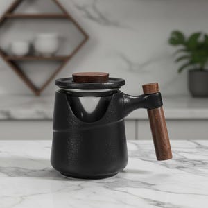 Puede incluir: Infusor de té negro con mango y tapa de madera. El infusor tiene un filtro de acero inoxidable y se apoya sobre una superficie de mármol. El mango y la tapa son de madera oscura. Diseñado para preparar té.