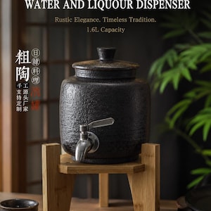 Peut inclure: Un distributeur d'eau et de liqueur en céramique noire d'une capacité de 1,6 L, doté d'un couvercle et d'un robinet en métal argenté. Le distributeur repose sur un support en bois clair. Le texte sur l'image indique : JAPANESE TRADITIONAL WATER AND LIQUOUR DISPENSER.