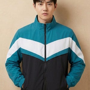 May include: A teal, white, and black track jacket with a full-length zip and a stand-up collar. The jacket features a chevron design across the chest and is made of a lightweight material. The jacket has two front pockets.