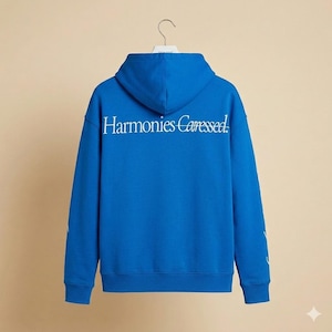 Könnte beinhalten: Ein königsblauer Kapuzenpullover mit dem weißen Aufdruck "Harmonies Caressed" auf dem Rücken. Der Kapuzenpullover hat eine Kapuze und lange Ärmel. Das Kleidungsstück hängt an einem weißen Kleiderbügel.