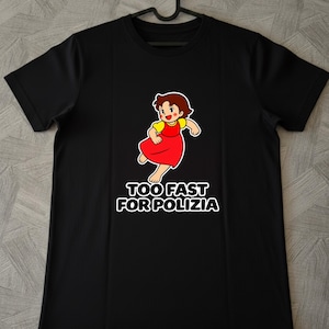 Può includere: Una t-shirt nera a maniche corte con la grafica di un personaggio dei cartoni animati dai capelli castani che indossa una maglietta gialla e un vestito rosso. Sotto il personaggio, il testo "TOO FAST FOR POLIZIA" è in bianco con bordo nero.
