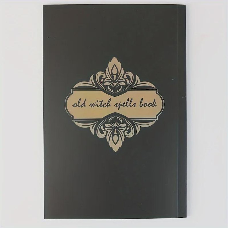 Pu&ograve; includere: Un libro rettangolare nero con un emblema decorativo dorato centrato caratterizzato da volute ornamentali. Il testo "old witch spells book" &egrave; stampato in corsivo nero all'interno del pannello centrale dorato della copertina.
