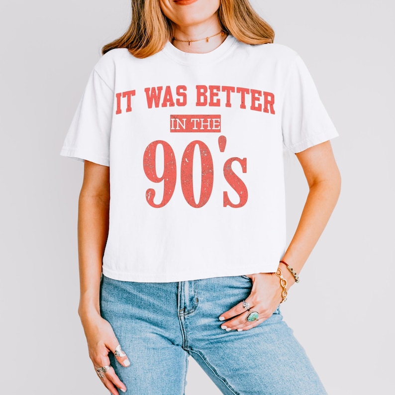 May include: A white short-sleeved t-shirt featuring the red distressed text IT WAS BETTER IN THE 90's printed on the front. The shirt has a crew neckline and a standard fit, paired with blue denim jeans that have a classic five-pocket design.