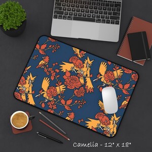 Può includere: Un tappetino da scrivania rettangolare con sfondo blu scuro e un motivo ripetuto di uccelli arancioni e fiori rossi. Il tappetino riporta il testo Camelia - 30,5 cm x 45,7 cm nell'angolo in basso a destra, indicandone le dimensioni.