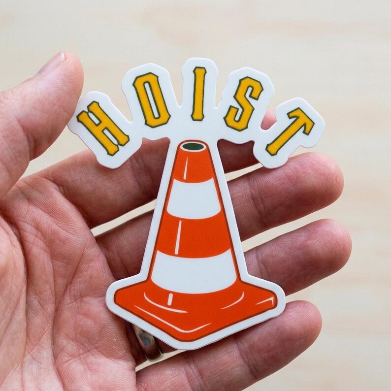Puede incluir: Una pegatina con un dise&ntilde;o de cono de tr&aacute;fico con la palabra "HOIST" en letras amarillas. El cono es naranja con rayas blancas. La pegatina se sostiene en una mano.