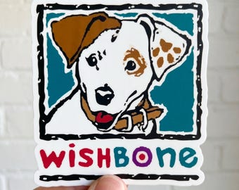 May include: A sticker featuring a dog illustration with brown and white markings, a red tongue, and a brown collar. The dog is set against a teal background within a black and white border. The word "wishbone" is written in red, purple, and teal.