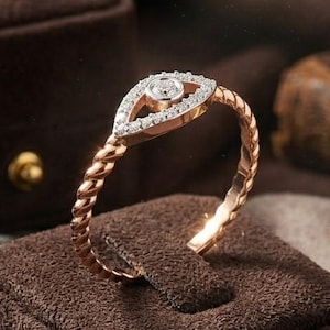 Könnte beinhalten: Ein goldenes Armband mit geflochtenem Band und einem tropfenförmigen Mittelstück, das mit kleinen Diamanten besetzt ist. Das Armband wird auf einem braunen Samt-Schmuckständer präsentiert, mit einer Samtbox und einem Kompass im Hintergrund.