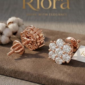 Könnte beinhalten: Roségoldene Blumen-Ohrstecker mit klaren Edelsteinen. Die Ohrringe werden auf einer braunen Oberfläche mit einer kleinen weißen Karte mit der Aufschrift "Riora" und dem Slogan "Shine with Elegance" präsentiert.
