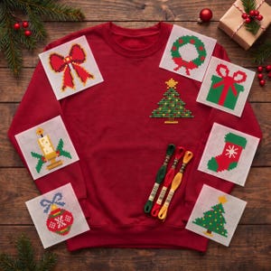 May include: A red crewneck sweatshirt featuring a small embroidered pixel-art Christmas tree on the chest. Surrounding the sweatshirt are six square paper patterns showing pixel-art holiday designs and three skeins of embroidery floss.