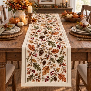 May include: A rectangular table runner featuring a cream-colored fabric base with a printed pattern of autumn leaves, pinecones, acorns, red berries, and small white flowers, bordered by a thin dark brown line along the edges of the textile.