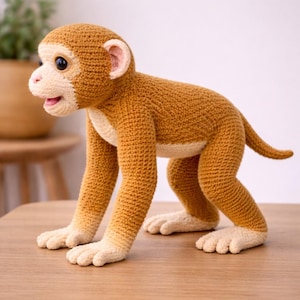 Op de afbeelding: Een handgemaakt gehaakt aap speelgoed in bruine en crèmekleurige tinten. De aap staat op alle vier, met een gedetailleerd gezicht, oren en staart. Het speelgoed staat op een houten tafel.