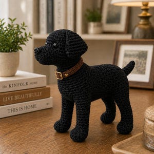 Könnte beinhalten: Handgefertigte schwarze Häkelhund-Figur mit braunem Halsband und goldener Schnalle. Der Hund steht auf einer Holzoberfläche. Die Figur ist ein dekoratives Element, möglicherweise für die Heimdekoration oder als Geschenk.