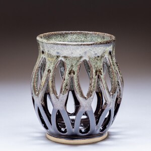 May include: A handcrafted ceramic vase with a unique openwork design. The vase features a speckled, light green and brown rim, transitioning to a dark, glossy base. The openwork pattern creates a lattice effect, adding visual interest to this decorative piece.