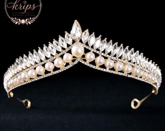 Könnte beinhalten: Ein goldfarbenes Diadem mit V-förmigem Design, verziert mit weißen Perlen und klaren, marquise-geschliffenen Kristallen. Die Krone hat einen zentralen birnenförmigen Kristall an der Spitze sowie ein feines Metallband und das Logo Krips Jewelry Studio.