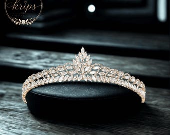 Könnte beinhalten: Ein Diadem mit einer spitzen Mitte und einem Band aus zahlreichen klaren, marquise-geschliffenen Kristallen in einem Metallrahmen. Das Logo von Krips Jewelry Studio ist in der oberen linken Ecke des Bildes zu sehen.
