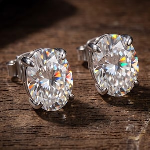 May include: A pair of stud earrings featuring oval-cut clear stones set in silver-toned metal prongs. Each stone displays a faceted surface that reflects light with rainbow-colored prismatic effects, secured with standard post-style earring backs.
