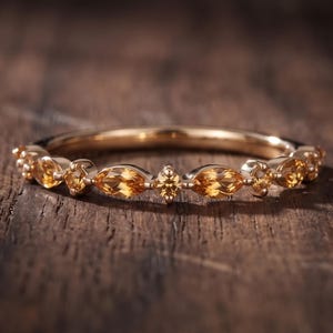 Peut inclure: Une bague en or ornée d'une série de pierres précieuses citrines jaunes alternant entre une taille marquise et une taille ronde le long de l'anneau. L'anneau en métal présente une finition polie et les pierres sont disposées symétriquement.