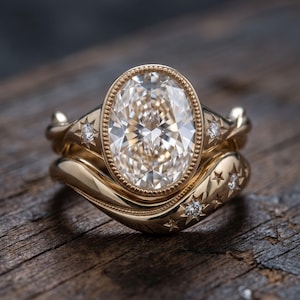 Puede incluir: Un conjunto de anillos de oro con una gran piedra central de corte ovalado rodeada por un engaste de cuentas. La banda y la alianza contorneada a juego están decoradas con motivos de estrellas grabados, cada uno con una pequeña piedra clara.