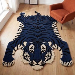 Könnte beinhalten: Ein tigerförmiger Teppich mit einem tiefblauen und schwarzen Streifenmuster sowie cremefarbenen Akzenten an Gesicht und Pfoten. Der Teppich ist in der Silhouette eines Tigers mit ausgestreckten Gliedmaßen und einem detaillierten Katzenkopf gestaltet.