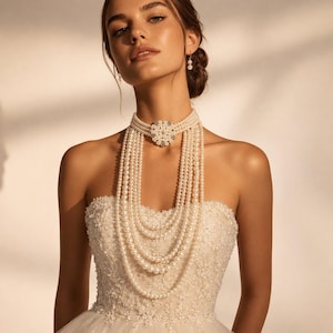 Peut inclure: Un collier de perles à plusieurs rangs doté d'une décoration centrale circulaire en forme de fleur avec des cristaux transparents. Le collier se compose de plusieurs couches drapées de perles blanches suspendues à un tour de cou.
