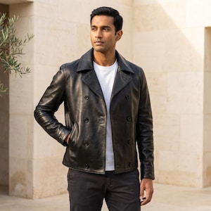 Puede incluir: Chaqueta de cuero negra con diseño de doble botonadura. La chaqueta tiene cuello con solapas, dos filas de botones y bolsillos laterales. La persona lleva una camiseta blanca y pantalones oscuros.