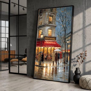 Op de afbeelding: Een verticaal ingelijst olieverfschilderij met een Parijs straatbeeld bij nacht. Het kunstwerk toont een felverlicht café met een rode luifel, goudkleurige ramen en figuren die over een natte, reflecterende straat lopen onder een blauwe lucht.