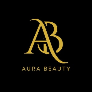 May include: Gold-colored logo on a black background. The logo features the intertwined letters "A" and "B" in a stylized script. Below the logo, the words "AURA BEAUTY" are displayed in gold.