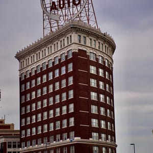 Può includere: Un alto edificio in mattoni a più piani con una facciata curva e numerose finestre rettangolari. Sul tetto si trova una grande insegna metallica illuminata con la scritta WESTERN AUTO all'interno di una cornice circolare su una struttura.