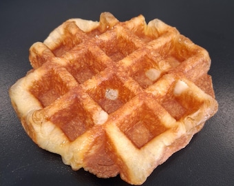 May include: A golden-brown waffle with a grid pattern, resting on a dark surface. The waffle has a crispy exterior and a soft interior, perfect for breakfast or brunch. The waffle is a classic breakfast food.