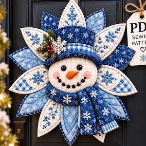 Puede incluir: Un adorno de pared de tela acolchada con forma de muñeco de nieve, con sombrero de copa azul, bufanda azul y un borde de pétalos en forma de estrella con bordados de copos de nieve. Una etiqueta blanca muestra el texto PDF SEWING PATTERN.