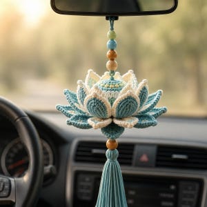 May include: A hanging car ornament featuring a crocheted lotus flower in shades of teal, cream, and light blue. The flower is suspended by a string of wooden and colored beads, with a long teal tassel hanging from the bottom of the lotus bloom.