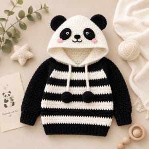 May include: A black and white crocheted hooded sweater featuring a panda face design on the hood with round ears, black eye patches, and pink cheeks. The body has horizontal stripes, long sleeves, and two dangling pom-poms on white drawstrings.