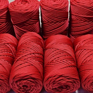 May include: A collection of multiple cylindrical spools of vibrant red cord arranged in a grid pattern. Each spool features a tightly wound, braided synthetic texture with a consistent deep red hue throughout the entire surface of the material.